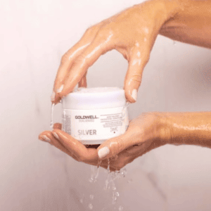 Hands holding a Goldwell hair product under running water, showcasing product quality and sleek packaging.