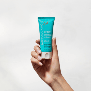 Hand holding a Moroccanoil product, highlighting its unique design and premium hair care branding.